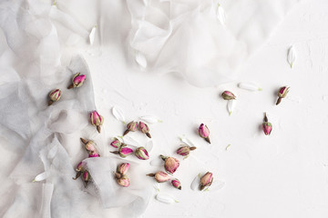 White feminine background with white and gray silk, white petals and dried roses. Copy space, slate background or texture. Concept.
