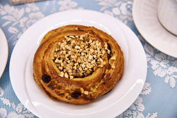 Hot bun with raisins and nuts on a white plate close-up.