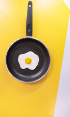 black pan and Fried egg on yellow and white background .