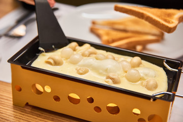 the girl tastes cheese raclette in a cafe. swiss food. cheese raclette with mushrooms on coupelles - special small skillet for a raclette