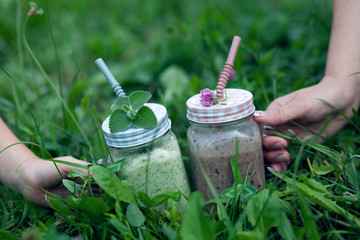 Two mag of smoothies  on a green grass. Drinking yogurt. Holding cup of smoothie.