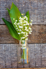 Bouquet of flowers beautiful smell lily of the valley or may-lily in glass vase on rustic old vintage wooden background. Garden in spring or summer concept. Close-up blossom twigs of Lilly of vally