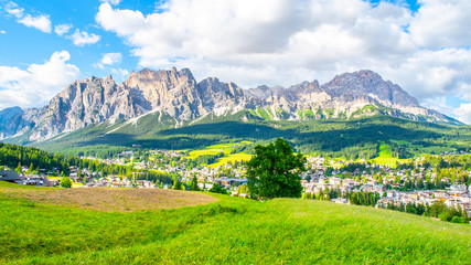Fototapeta na wymiar Panorama of Cortina d'Ampezzo with green meadows and alpine peaks on the background. Dolomites, Italy