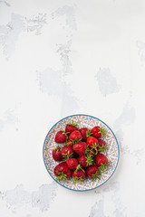 Fresh strawberries on light plate on white old concrete background. Top view.