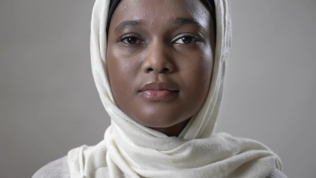 Young sad african muslim girl in hijab is looks up and watching at camera, religioun concept, grey background