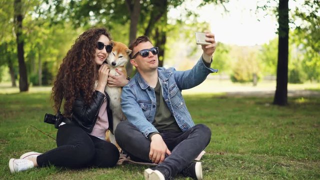 Popular blogger is recording video about himself, his wife and cute dog, man is holding smartphone, talking and looking at camera then on the woman and animal.