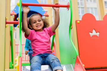 happy curly african american little kid sliding down from hill at playground