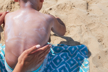 mother is putting on boy back a sunscreen on the beach.