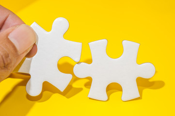 Obraz premium Man's hand holding a piece of blank white puzzle over yellow background.