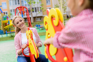 cropped image of girl riding on rocking horse with smiling mother at playground