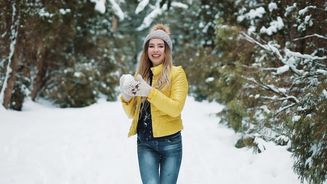 Charming girl plays with snowballs in the forest. Active young woman isthrowing snowball at the camera having fun outdoors during winter time