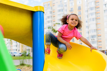 happy african american little kid sliding down from hill at playground