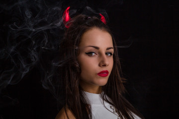 Fototapeta premium Portrait of young woman with red devil horns on head and cigarette smoke