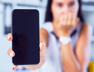 Young sad woman showing a blank smartphone screen. Focus on smartphone. Free space for your message.