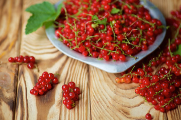 Red juicy currant lies on a wooden table and in plate.