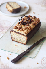 Almond Pear Loaf Cake covered with Chocolate Glaze, topped with Caramel Cream Cheese Frosting and decorated with Spicy Crumble, on light beige background. 