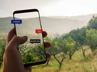 Augmented reality. Hand is holding a smart phone with AR app. Mobile information about walking or trekking trails in the forest.