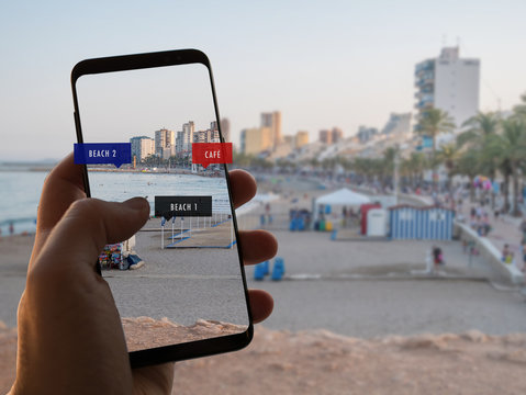 Augmented reality. Hand is holding a smart phone with AR app to check information on the beach on holiday or vacation.