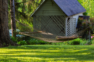 A white hammock in a yard with green grass and little shed.
