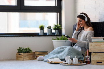 Portrait of beautiful smiling young woman with headphones indoors listening music