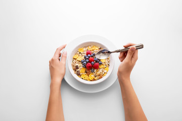 Young woman eating muesli cereal breakfast with berry fruit in a white bowl viewed directly from...