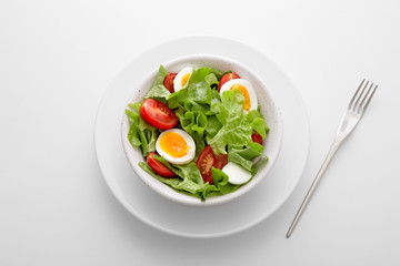 Fresh salad meal with letuce, eggs and tomato in a white bowl with a fork on the side viewed directly from above. Fresh organic vegetable snack viewed from above. Top view. Copy space