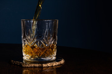 Whiskey being poured into a crystal tumbler from an angle on a dark wooden table