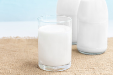 Two glass bottle and a cup of milk on the sackcloth with blue background. with copy space for text.