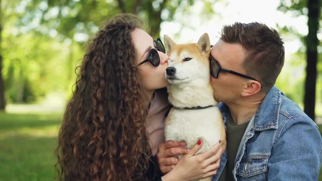 Slow motion of cheerful people kissing and caressing lovable dog touching its fur while animal is enjoying love and care. Young family is spending free time in park.