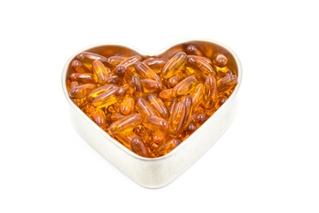 Fish oil capsules in a heart shape plate isolated on white background, vitamin D supplement, selective focus