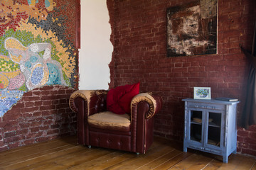 Interior of the room with an old leather armchair and a brick wall
