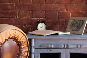 Desk clock with a book on a wooden cupboard against a brick wall background