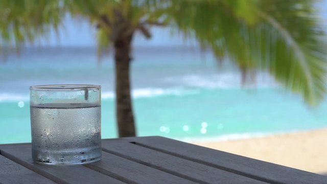 Wasserglas auf Tisch vor Strand Meer und Palme