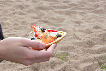 Fototapeta na wymiar slice of pizza in hand on the sand background on the shore