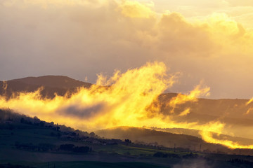 Obraz premium Low clouds over a rolling landscape at sunset