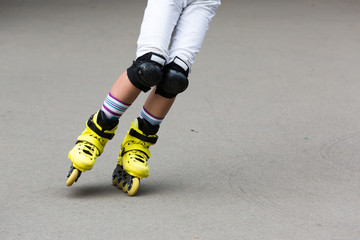 Close up beautiful slim legs of young girl in white shorts wearing roller skating in a sunny day in summer in the park. Knee protectors. Bright yellow rollers