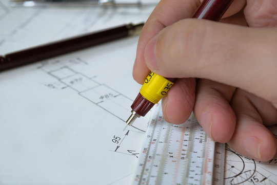 Man holding technical pen and working on a hand drawn technical drawing.
