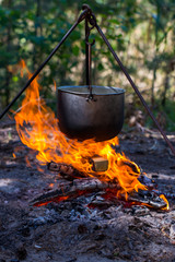 Tourist pot hanging over the fire on a tripod. Cooking in the campaign