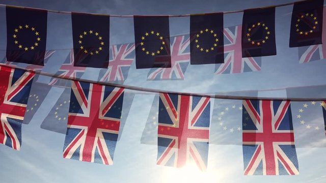 UK Union Jack flying with EU flag bunting flying in double exposure backlit against sunset light