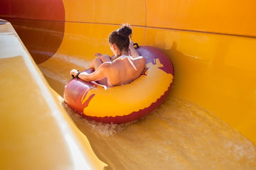 Young woman in bikini on a rubber inflatable float back on a water slide, playing and having a good...