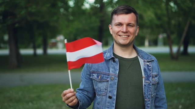 Slow motion portrait of proud Austrian citizen waving official flag of Austria, smiling and looking at camera. National pride, travellers and patriotism concept.