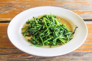 Green vegetables, fried oyster sauce Put a white plate on an old wood table.