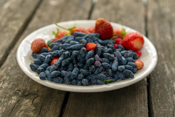 Summer berries - strawberries and honeysuckle on a wooden base in sunny weather. Still life, with fruit assorted platter with lot ripe appetizing strawberry and honeysuckle view closeup