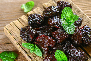 Prunes with mint leaves in a bowl on an old wooden table.
