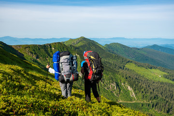 Adventurers with backpacks stands on green mountain slope