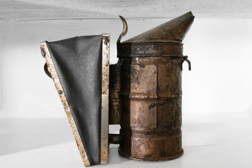 Rusty, dusty and very old bee smoker placed on white shelf