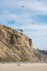 Fototapeta na wymiar Parachutes and gliders take flight over the beach and cliff
