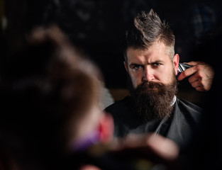 Reflexion of barbers hand with hair clipper trimming nape of client. Hipster bearded client getting...
