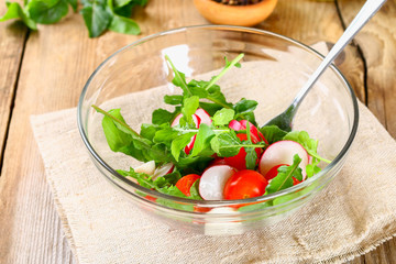 Vegetarian salad of arugula, tomato, radish and mozzarella cheese on an old wooden table.
