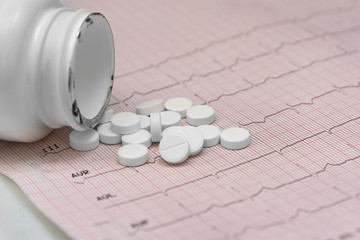 Pills canister with piills on an electrocardiogram on white background